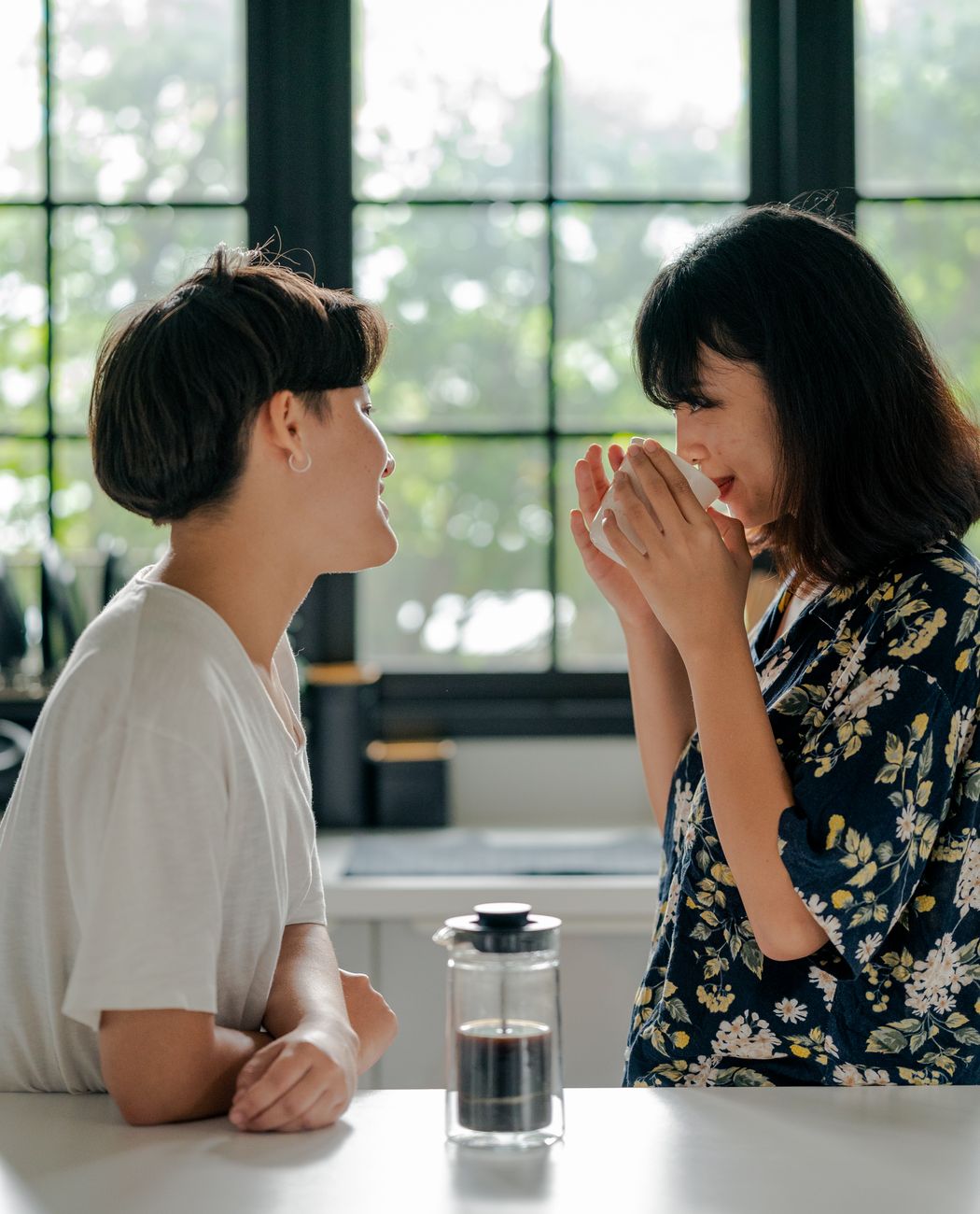 Two women sharing a joyful moment over morning coffee in a cozy kitchen setting.
