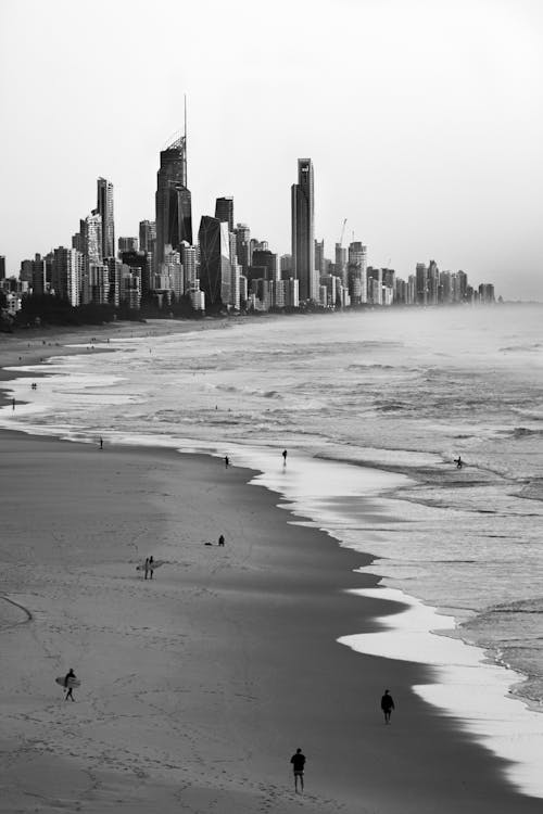 Grayscale Photo of People on Beach Against City Skyline