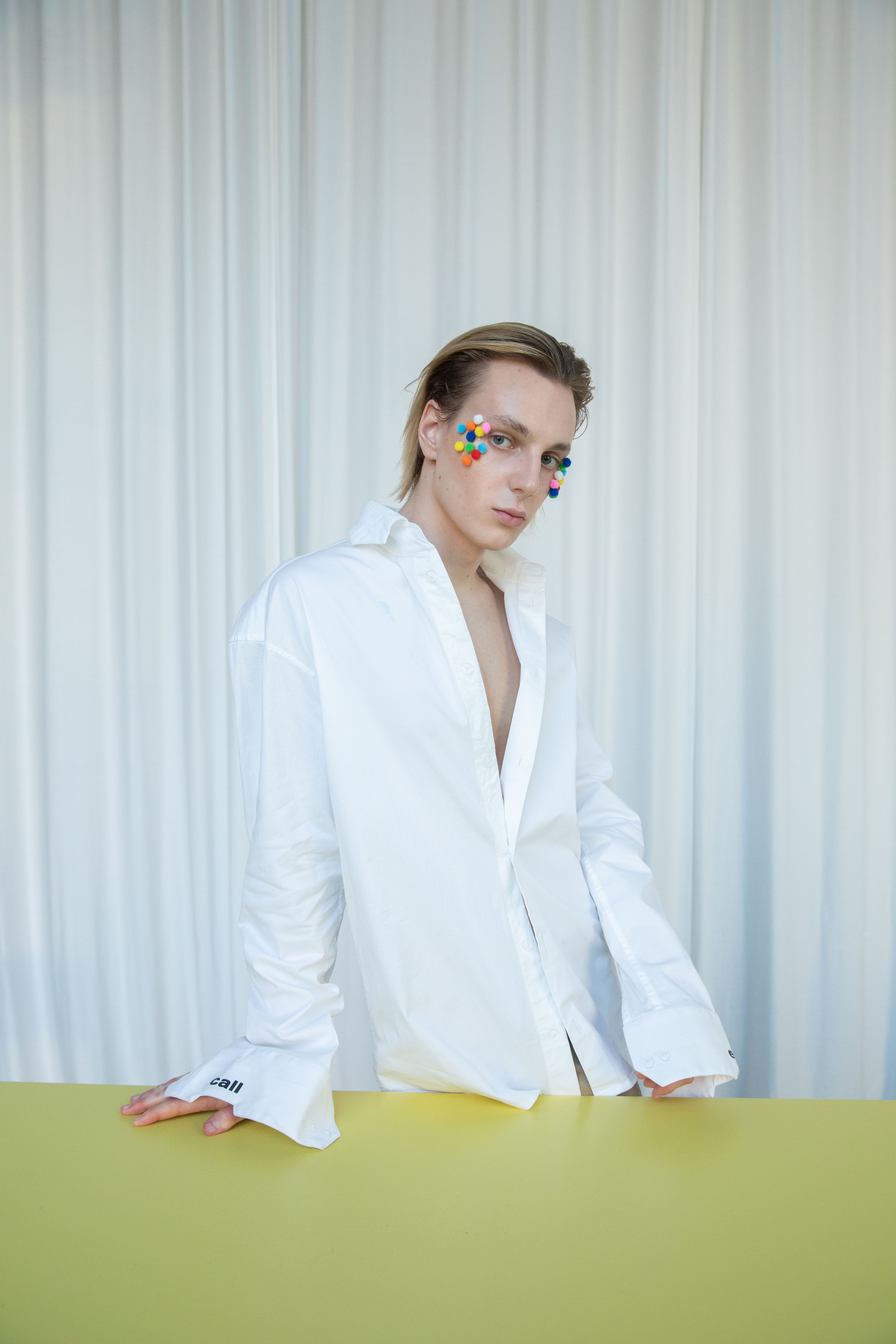 Stylish model in white shirt showcasing colorful artistic makeup, captured in a bright studio.