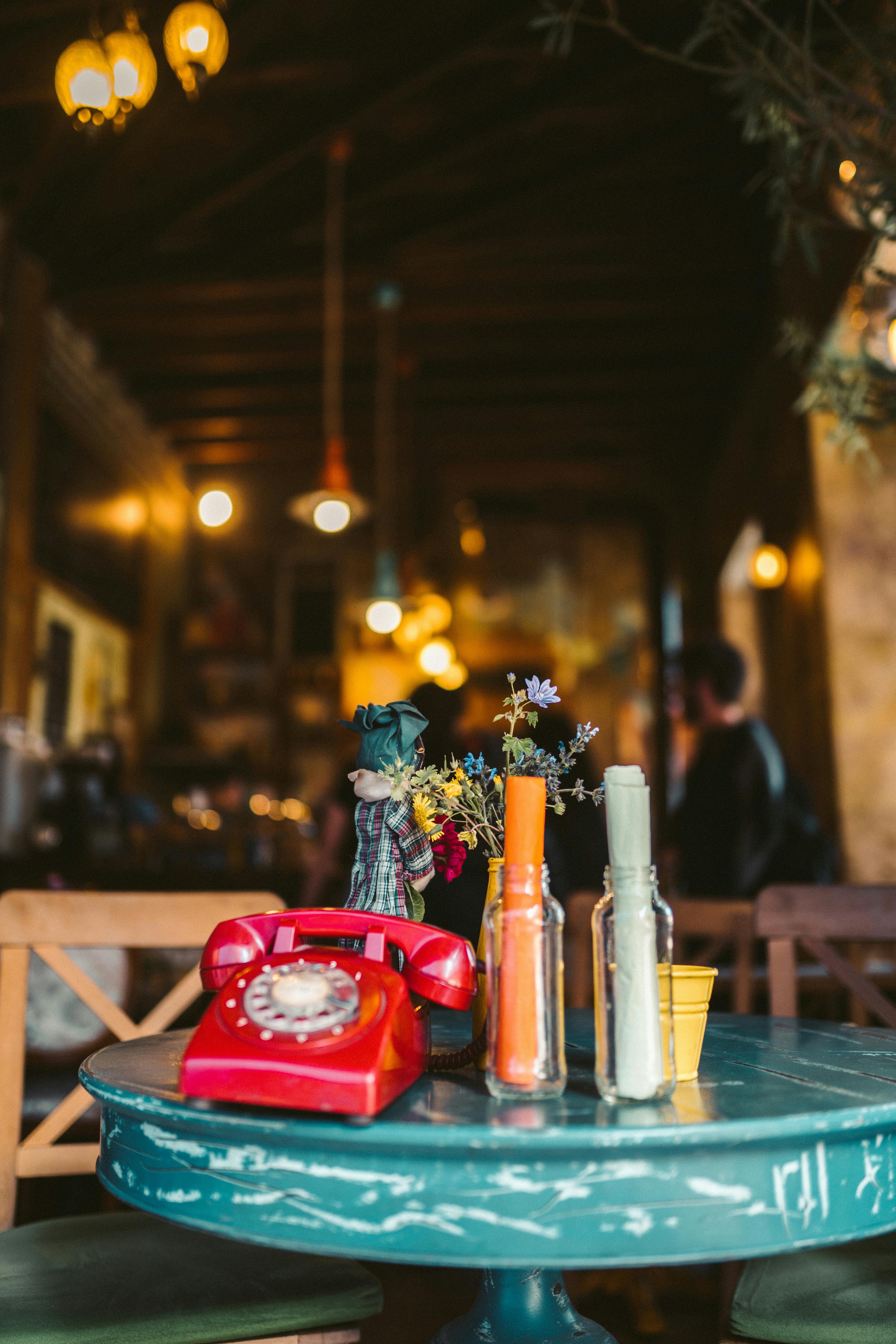 这家咖啡厅内部装饰复古舒适，蓝色桌子上摆着一台红色旋转电话
