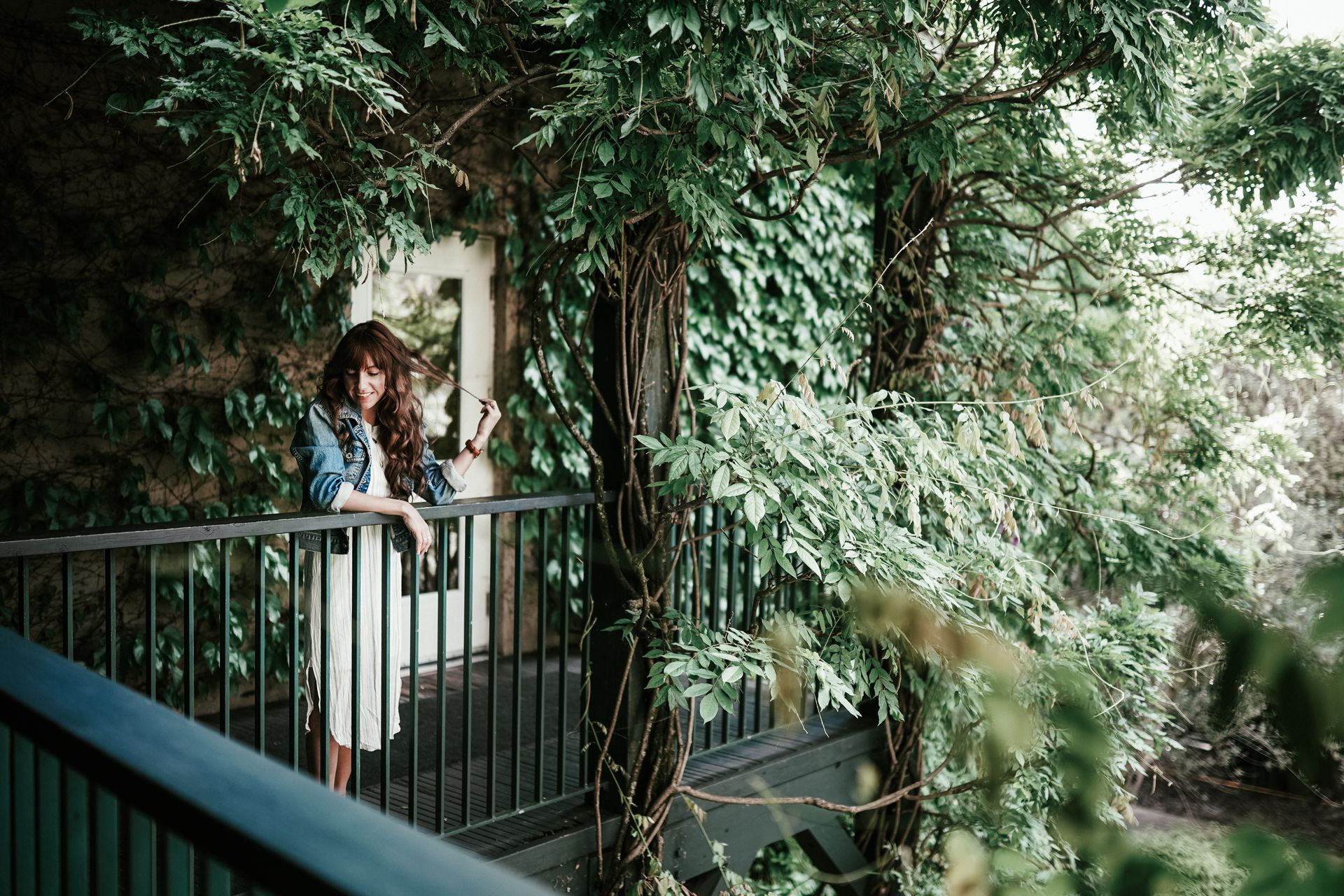 A woman enjoys a serene moment on a balcony surrounded by lush green foliage.