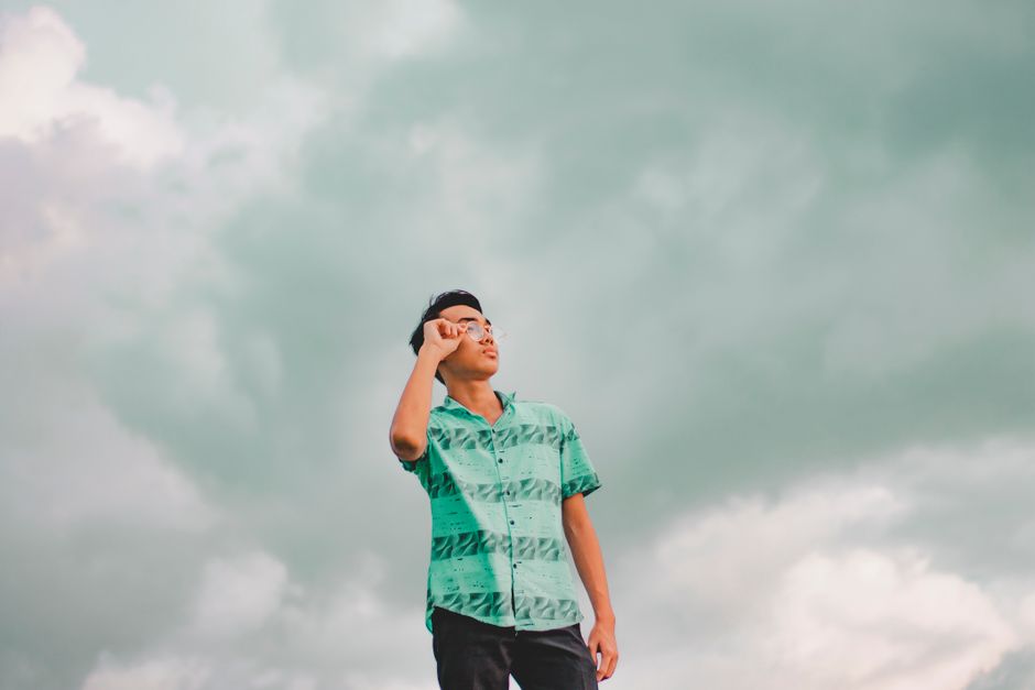 若い男性が曇り空の下、屋外で眼鏡を調整しています。