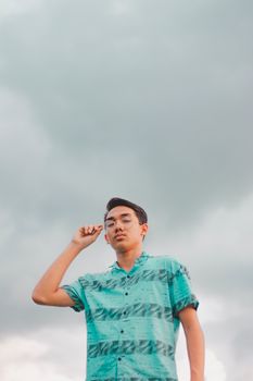 一位戴着眼镜的年轻人自信地以多云的天空为背景摆出姿势