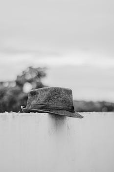 Black and white photo of a fedora hat on a fence, evoking a vintage, minimalist style.