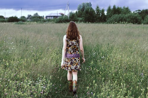 Woman in Floral Dress Walking on Grass Field