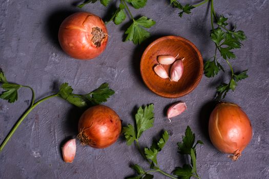 Aerial view of onions, garlic, and parsley on a rustic background, ideal for culinary themes.