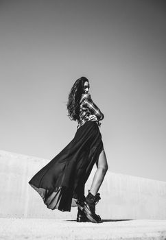 Fashion model poses with flowing dress under clear sky in black and white.
