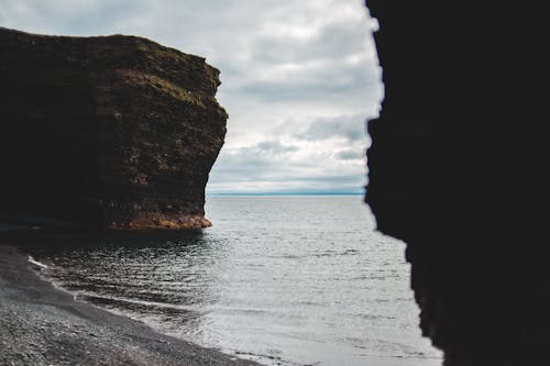 Overcast sky covered with dense clouds above dark brown cliff on rocky coast of calm reservoir