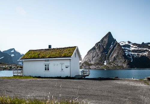 Free A picturesque Nordic cabin with grass roof by a serene mountain lake in Nordland, Norway. Stock Photo