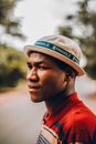 Side view of serious frowning African American male standing on street with blurred green trees