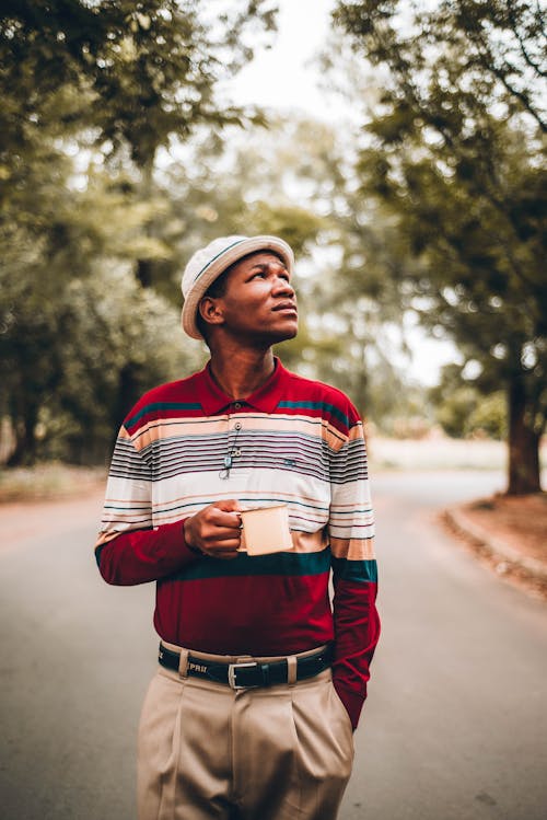 Serious black man in stylish outfit with cup in park