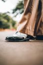 Crop legs of anonymous person wearing classy white and black brogue shoes and pants standing in green park