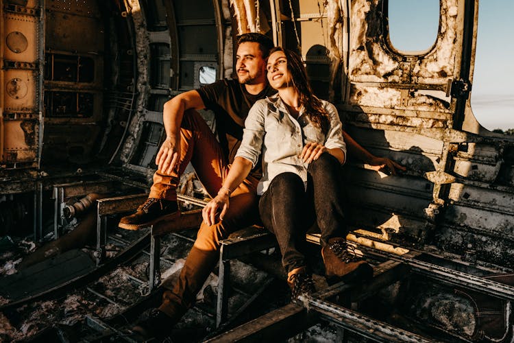 Dreamy Couple Of Travelers Resting On Aged Damaged Airplane Surface