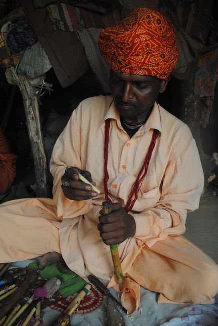 South Asian man crafting a traditional wooden flute, wearing vibrant attire and turban.