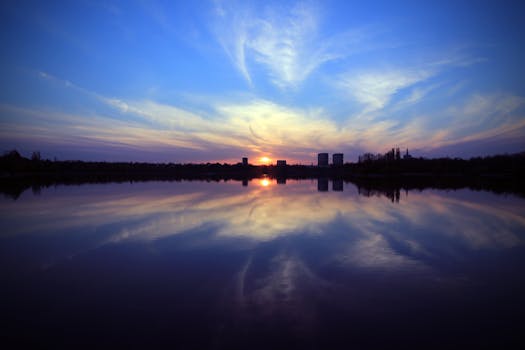 Peaceful sunset over a lake with city skyline reflection and colorful sky.