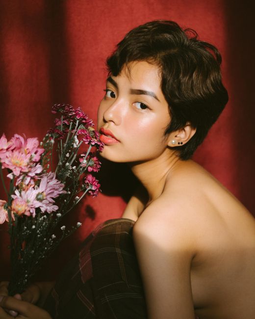 A captivating portrait of a woman with short hair holding flowers against a red background, capturing elegance and beauty.