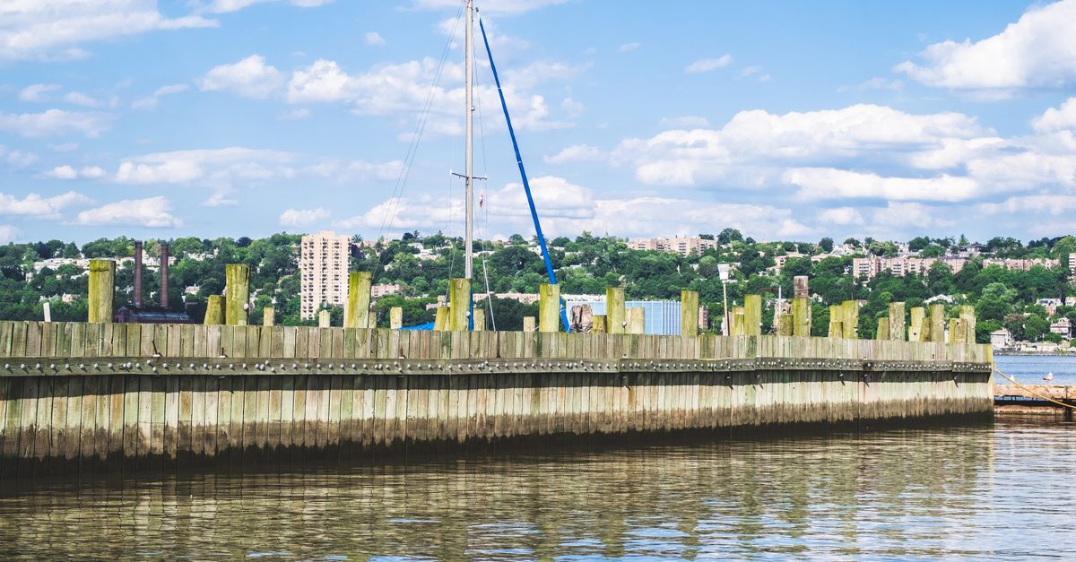 Tranquil water reflection and wooden pier under a vibrant blue sky in Alpine, New Jersey.