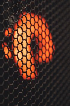 Closeup of blurred red lamp glowing with bright light inside of black metal grid of modern equipment in contemporary studio