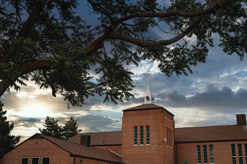 Free Exterior of small church constructed of brown brick walls near green trees under grey sky covered with clouds Stock Photo
