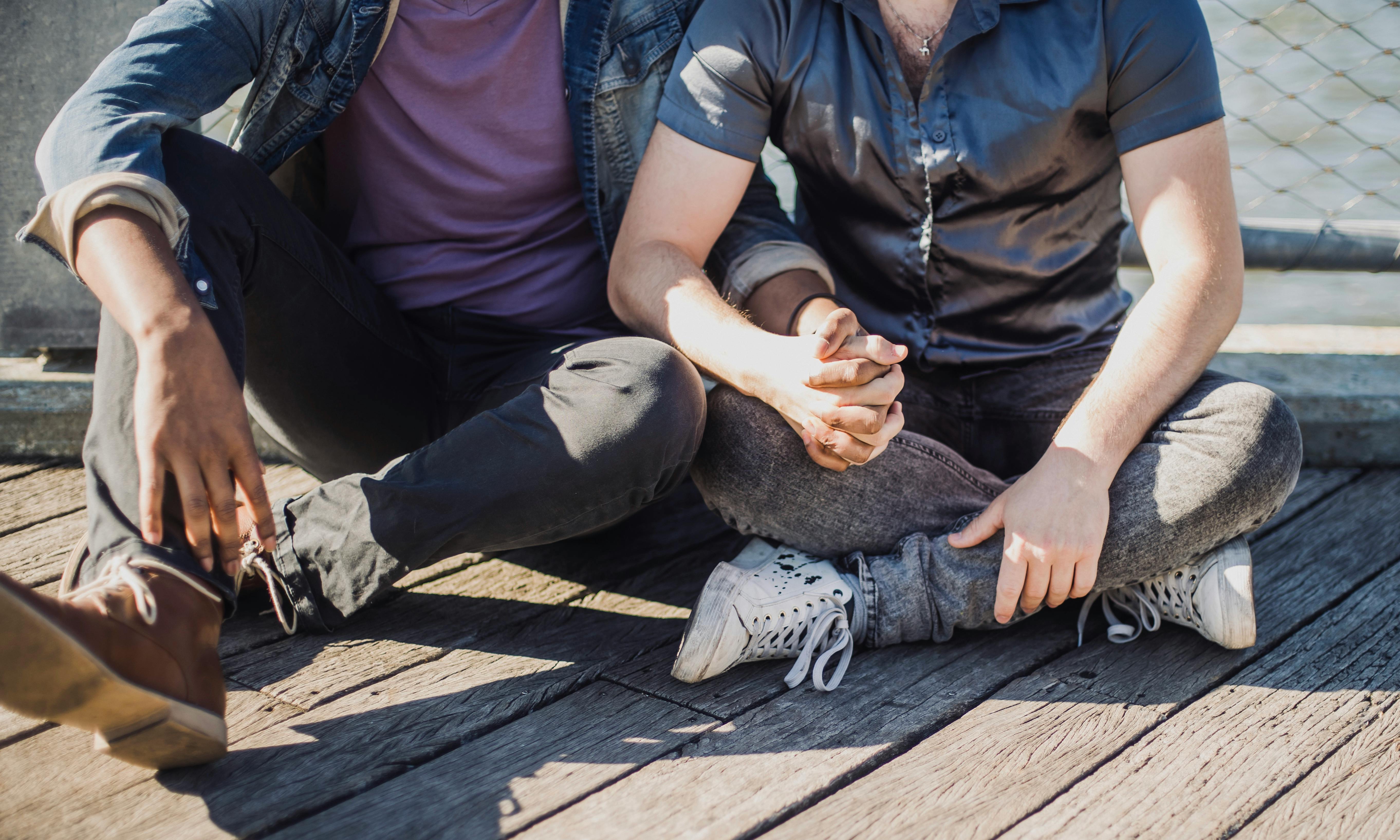 two men sitting and holding hands