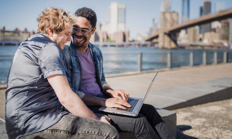 Two Men Sitting Outside With A Laptop