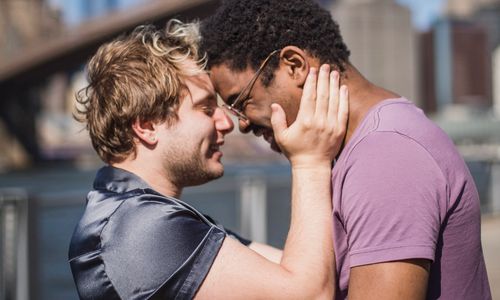 Free A loving moment between an interracial gay couple embracing outdoors with an urban backdrop. Stock Photo