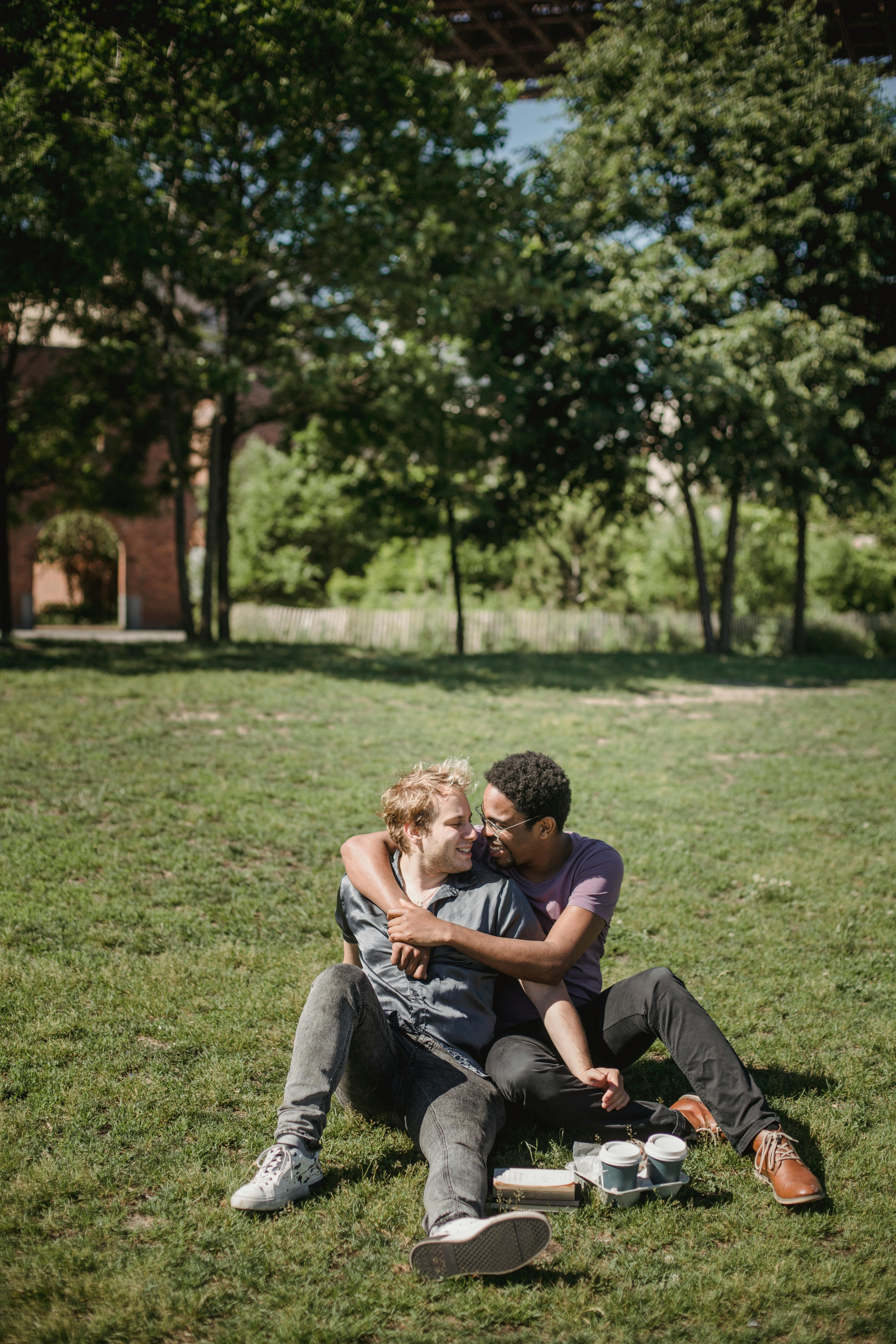 two men sitting on the grass and being affectionate