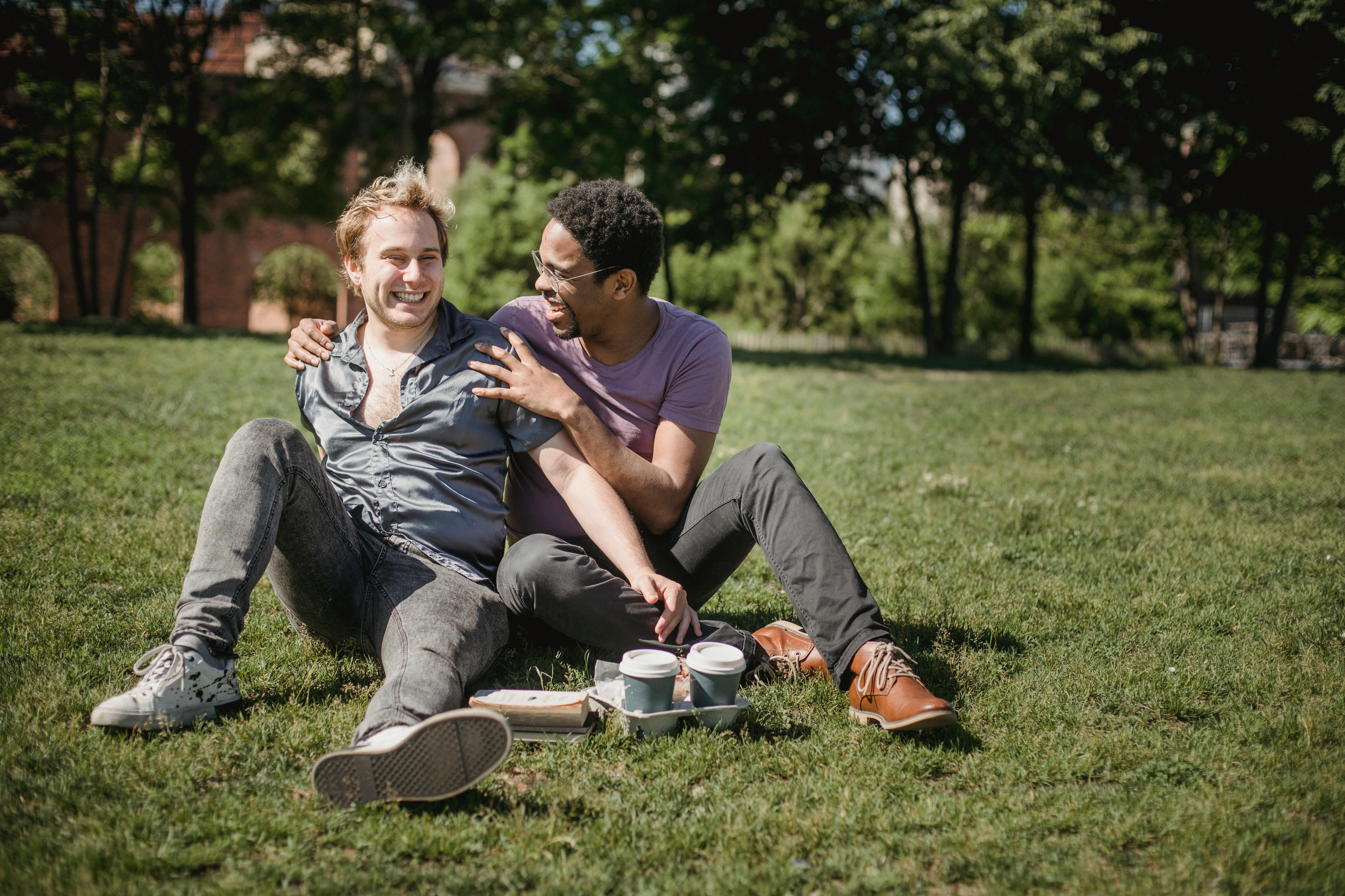 two men sitting on the grass and being affectionate