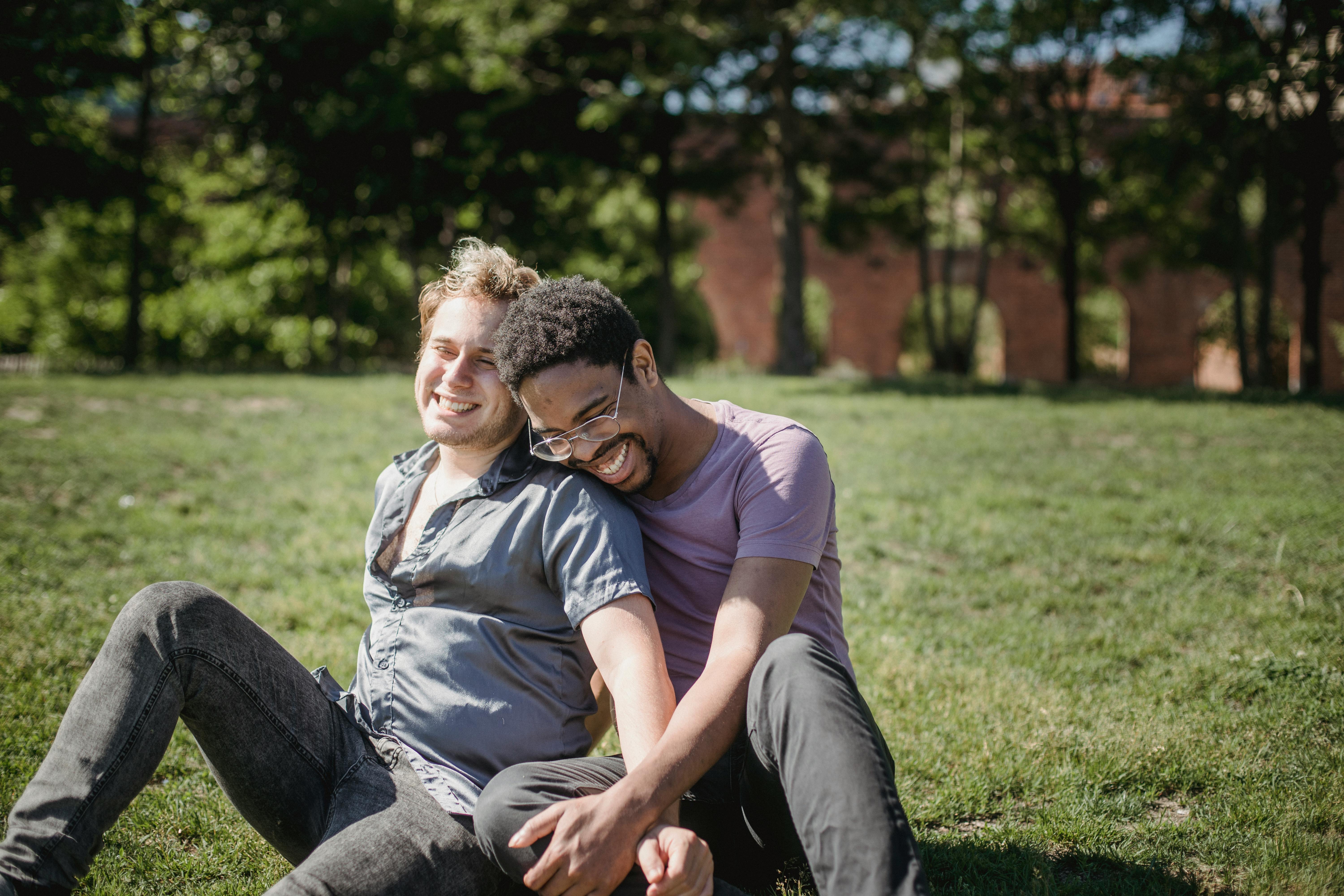 two men sitting on the grass and being affectionate