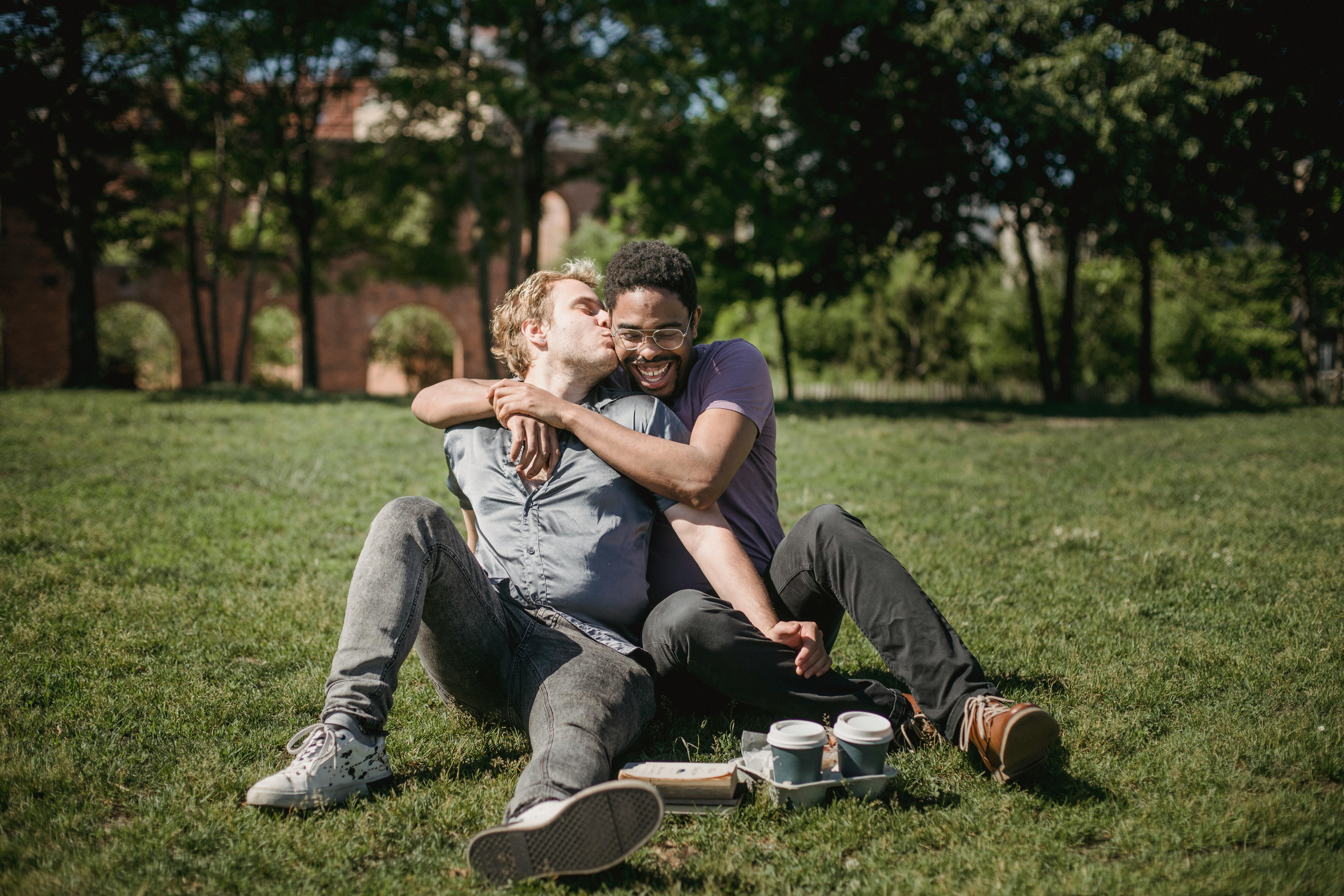 two men sitting on the grass and being affectionate