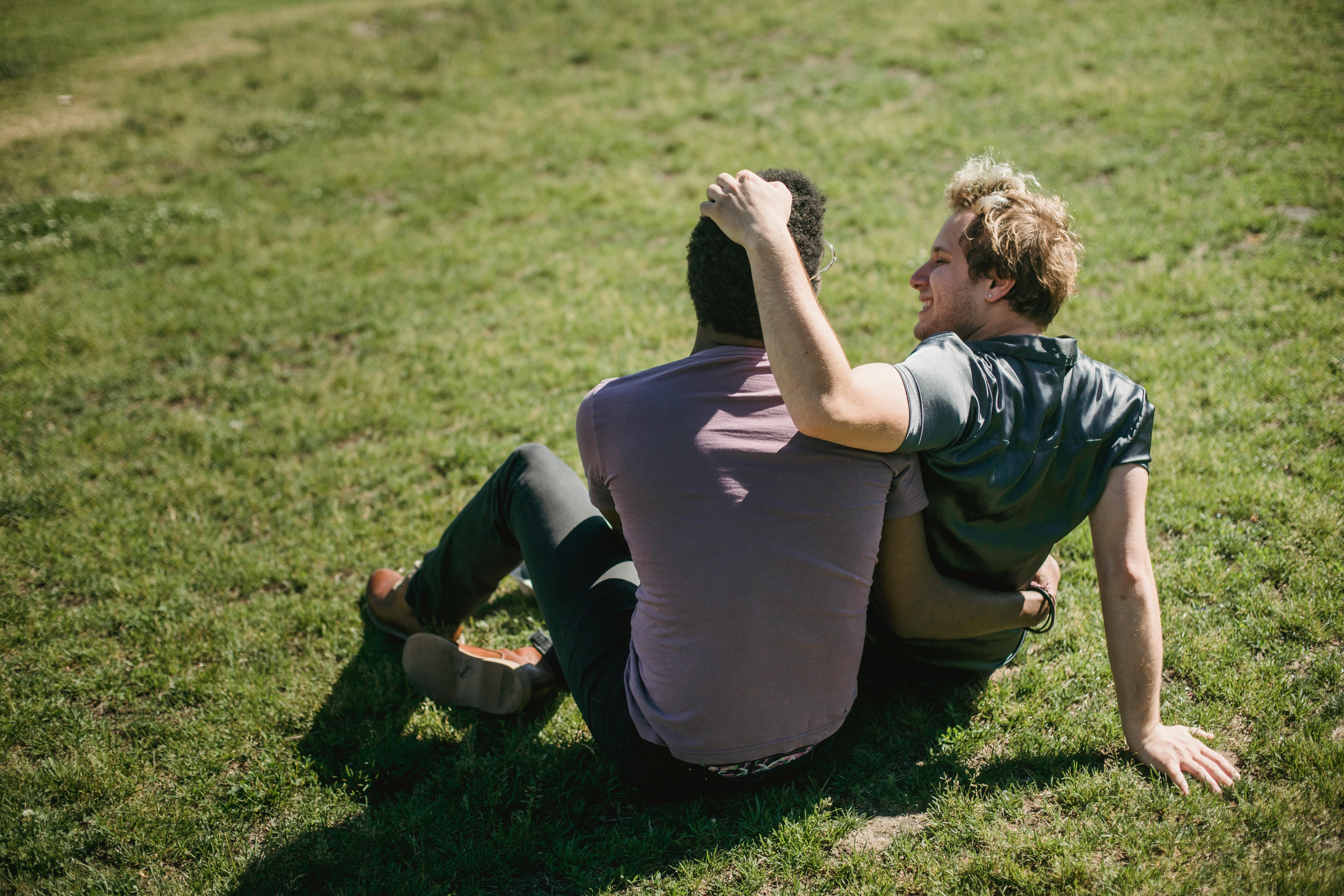 two men sitting on the grass and being affectionate