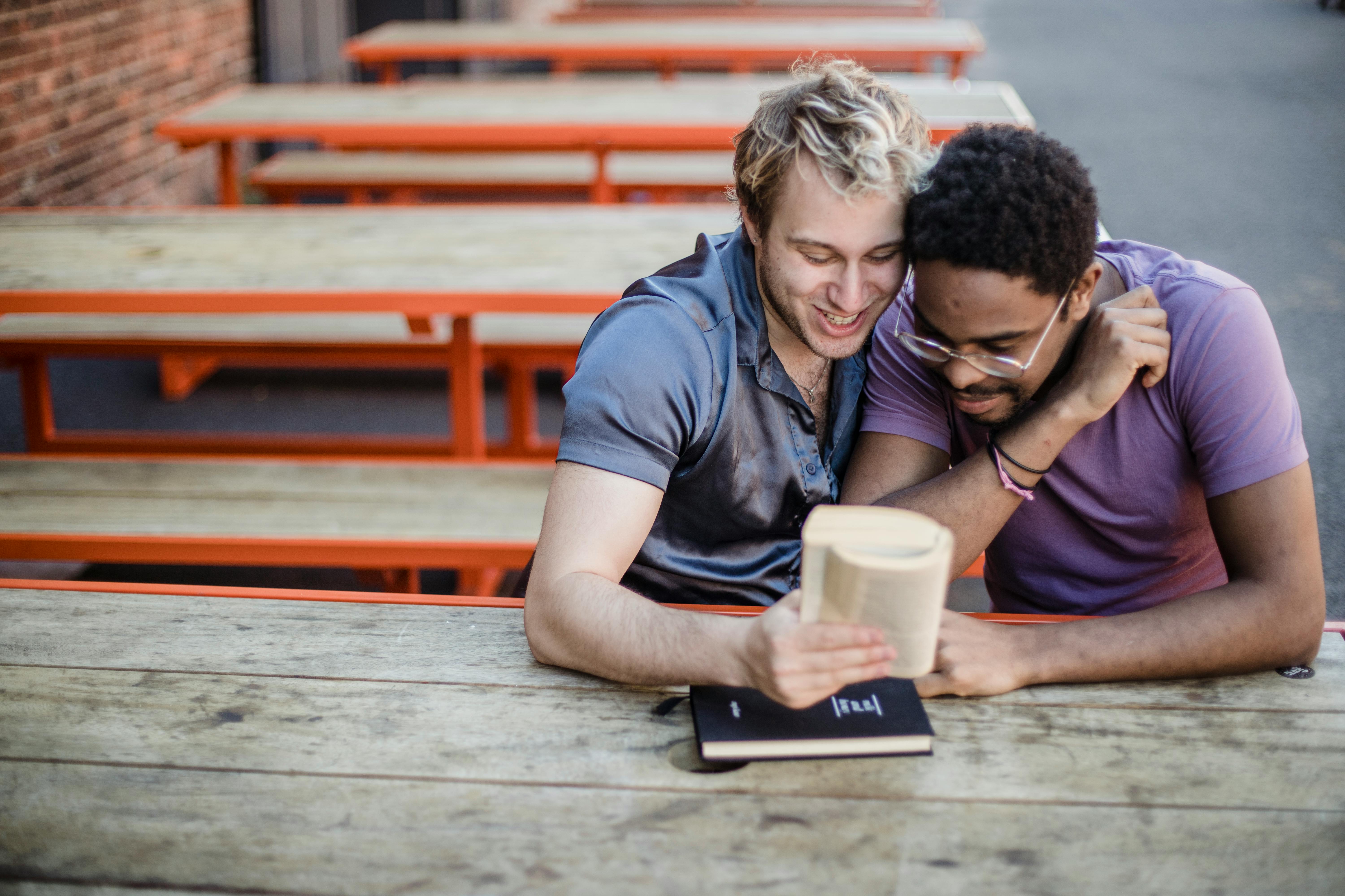 two men sitting together and reading a book