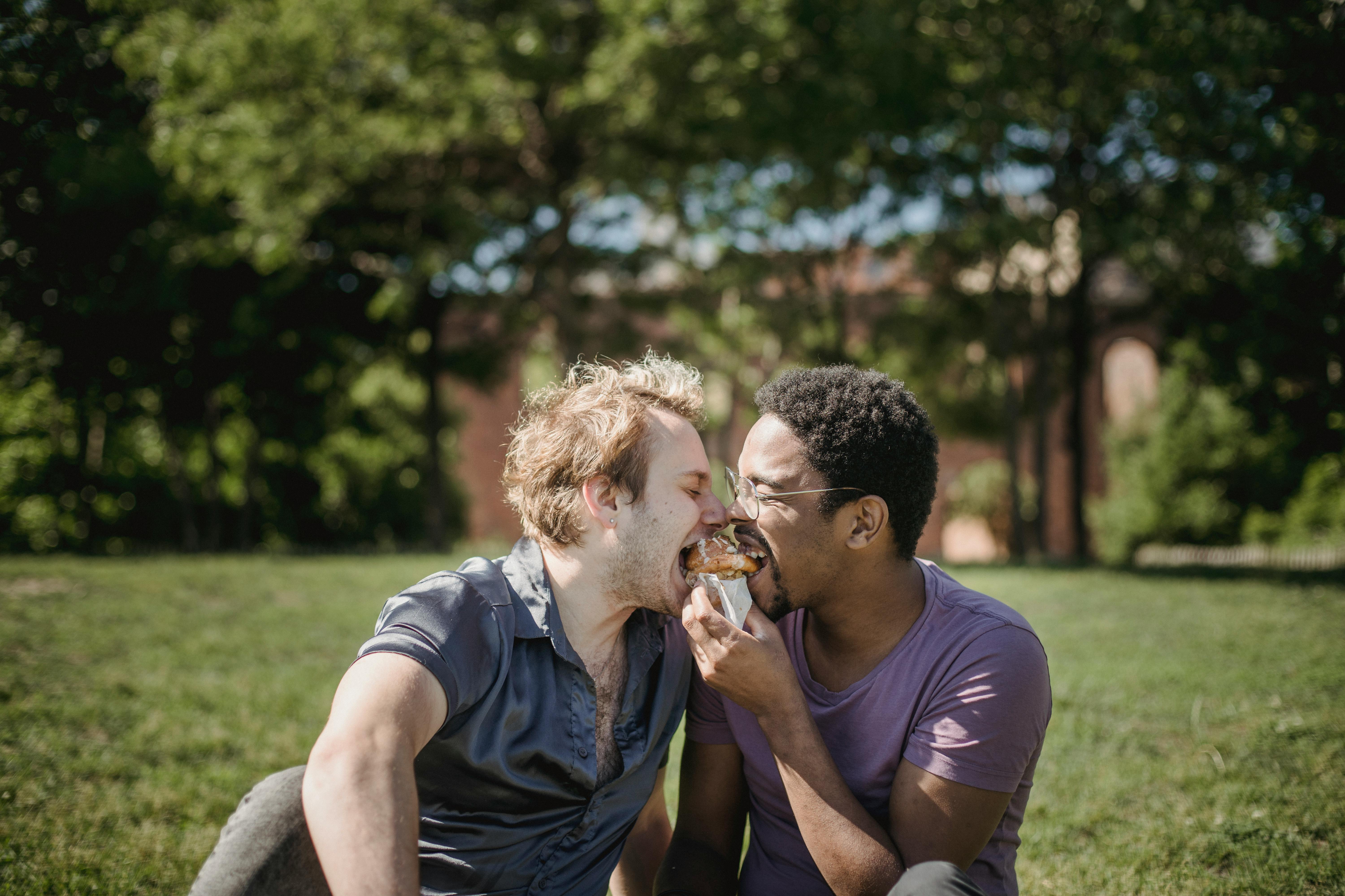 two men sharing food and sitting on the grass