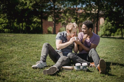 Two Men Sitting on the Grass and Sharing Food