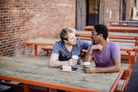 两个男人坐在户外的桌子旁，一起喝咖啡，展现着友谊与联系