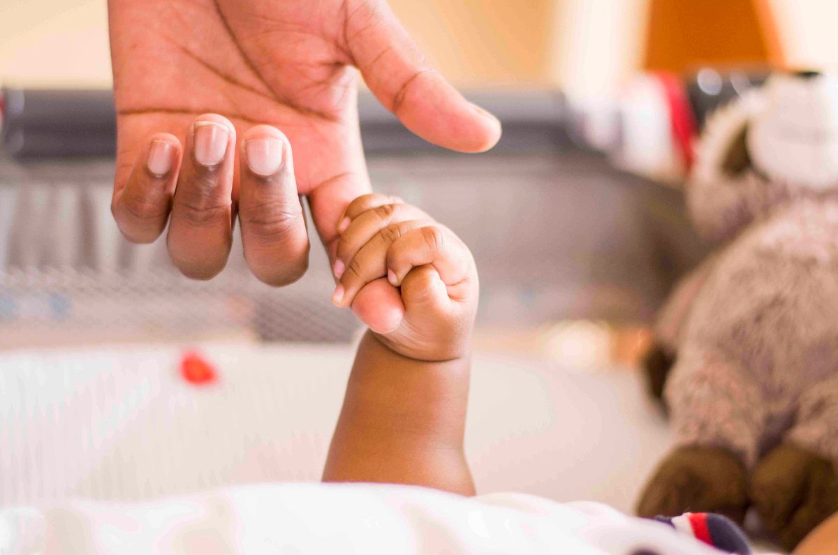 Mão de pai negro segurando mão de bebê simbolizando dúvidas sobre pensão socioafetiva