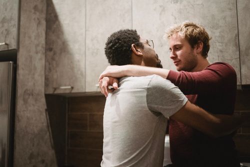 Free A tender moment between an interracial gay couple embracing indoors, showcasing affection and togetherness. Stock Photo