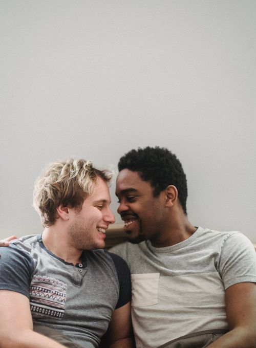 Free Interracial gay couple lovingly embracing and smiling indoors, depicting happiness and togetherness. Stock Photo