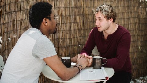 Interracial gay couple holding hands and enjoying coffee together at an outdoor cafe.