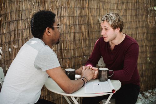 Free Interracial gay couple holding hands and enjoying coffee together at an outdoor cafe. Stock Photo