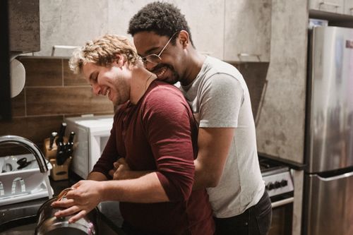 Free Happy interracial gay couple embracing in a cozy kitchen, sharing affection and warmth. Stock Photo