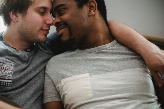 A tender moment shared by an interracial gay couple embracing affectionately indoors.