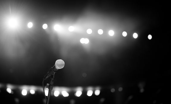 A dramatic black and white photo of a microphone onstage with bright concert lights.