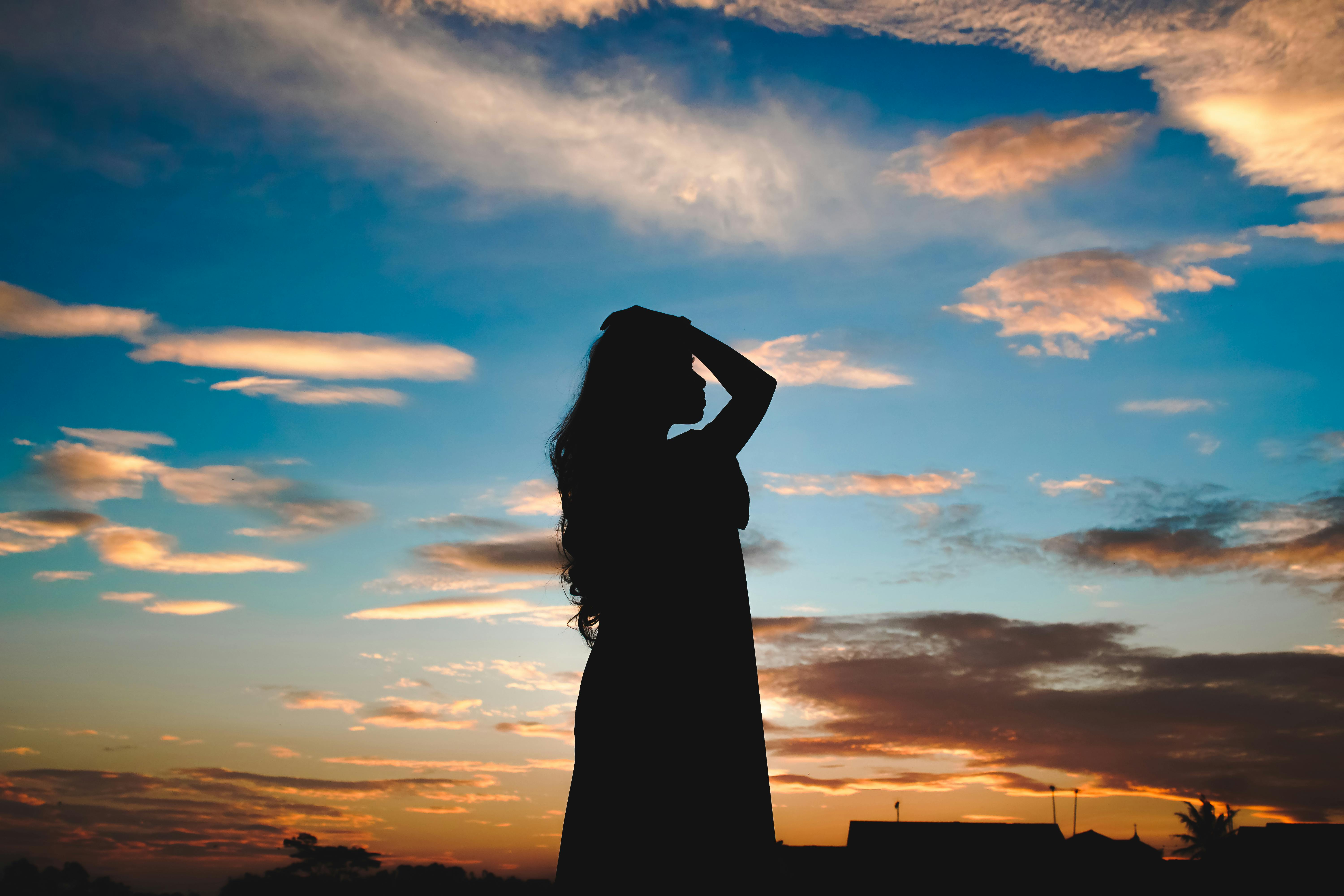 Silhouette of a woman touching her hair against a colorful sunset sky, capturing serene beauty.