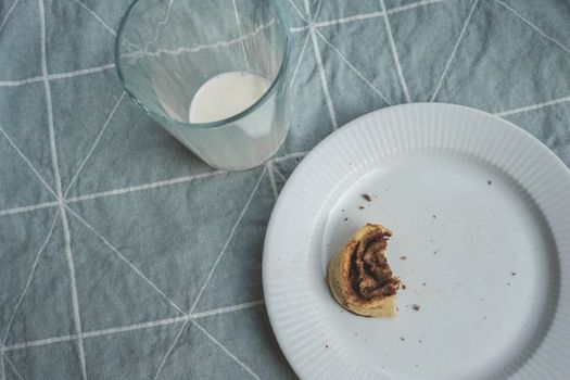 A half-eaten pastry and a glass of milk on a table with a cloth.
