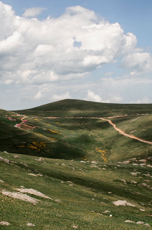 Scenic view of green mountain valley with stones and road on blue sky with fluffy clouds