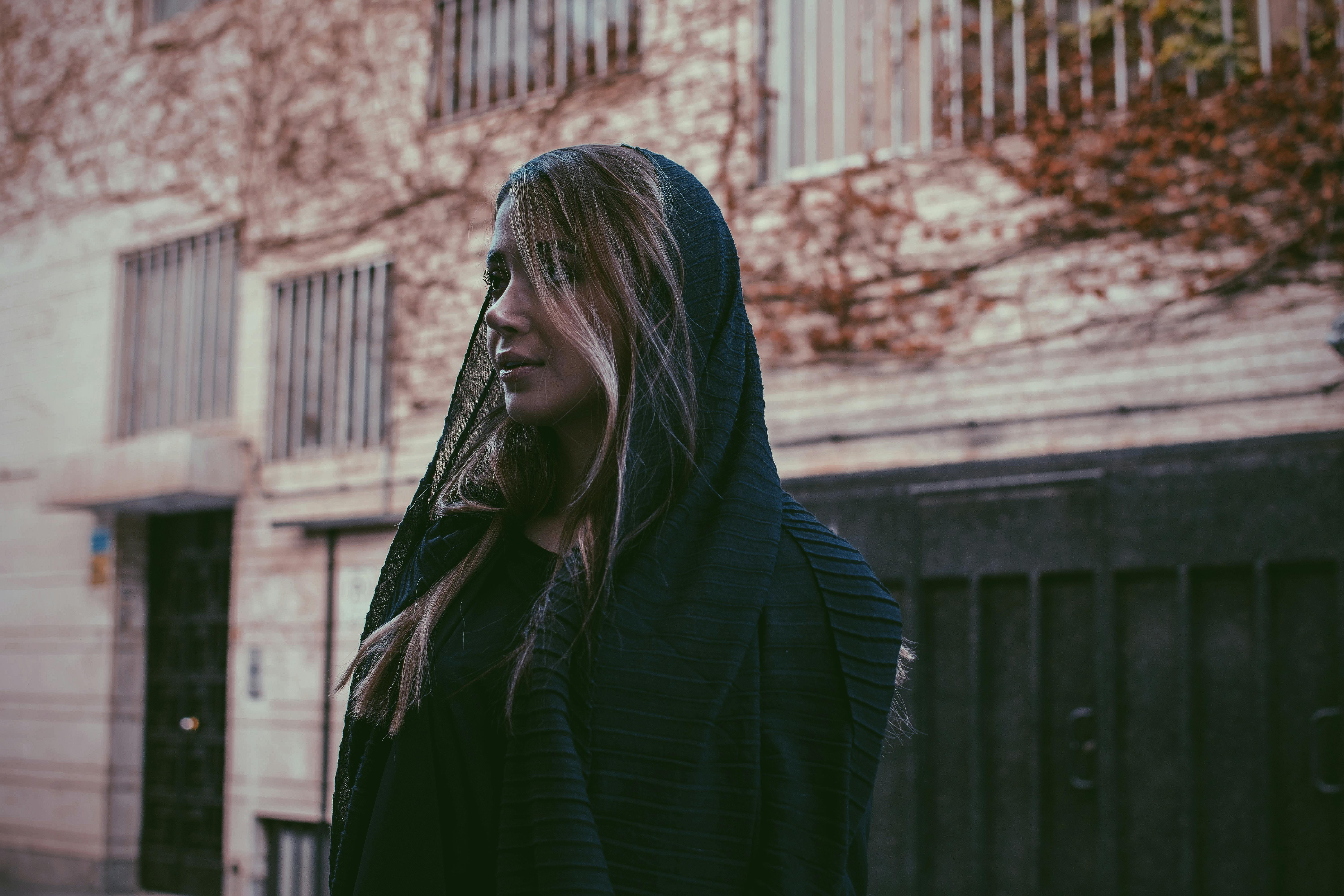 一位戴着黑色面纱的女子，沉思着站在城市街道上，显得体贴而优雅