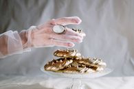 一只优雅的手戴着透明手套，从玻璃蛋糕架上拿起金色的蛋白酥皮甜点