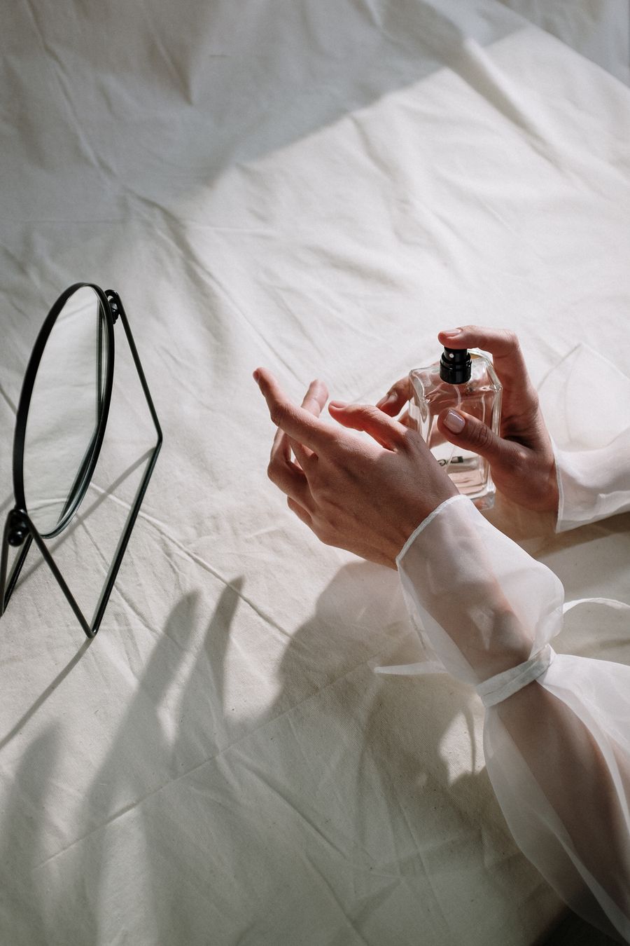 Hands holding a glass bottle against soft white cloth &mdash; photo by cottonbro studio on Pexels