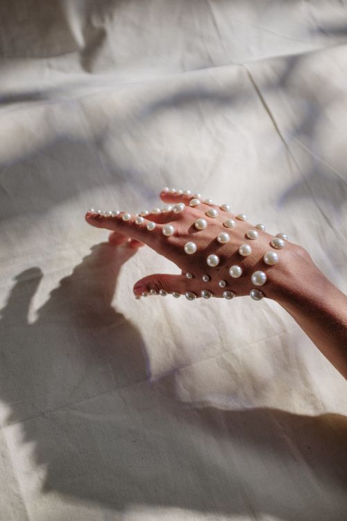 Free A graceful hand covered in pearls resting on a textured fabric with soft lighting and delicate shadows. Stock Photo
